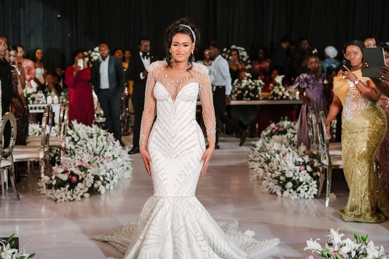 Bride in white beaded mermaid wedding dress walking down aisle at formal indoor wedding ceremony with white floral arrangements