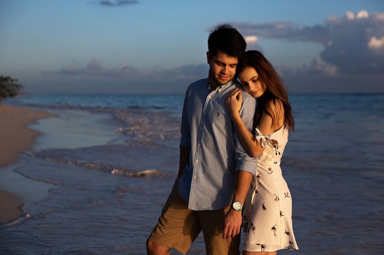 Couple embracing on a beach at sunset, with waves and sky in the background