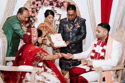 Bride and groom exchanging documents at traditional Indian wedding ceremony with family members and floral decorations in background