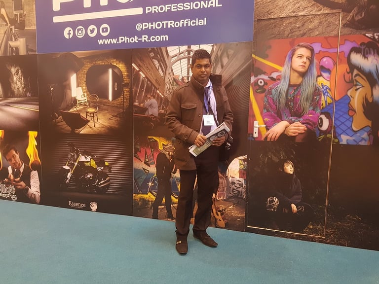 Man in business attire standing in front of a photography exhibition display with colorful portrait images and professional branding