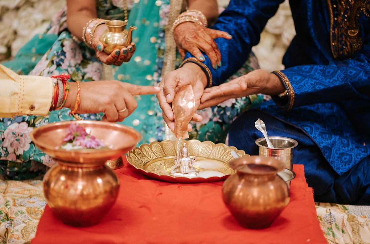 Hindu couple performing sacred ritual pouring water during wedding ceremony with hands joined over decorative vessel — Hindu wedding cinematography Tanzania