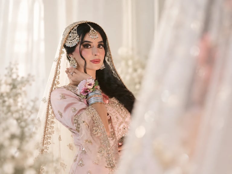 Woman in elegant pink bridal outfit with ornate beaded veil and traditional jewelry, posed in luxurious wedding setting