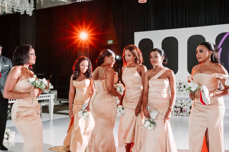 Group of bridesmaids in matching blush-colored gowns holding bouquets at wedding celebration